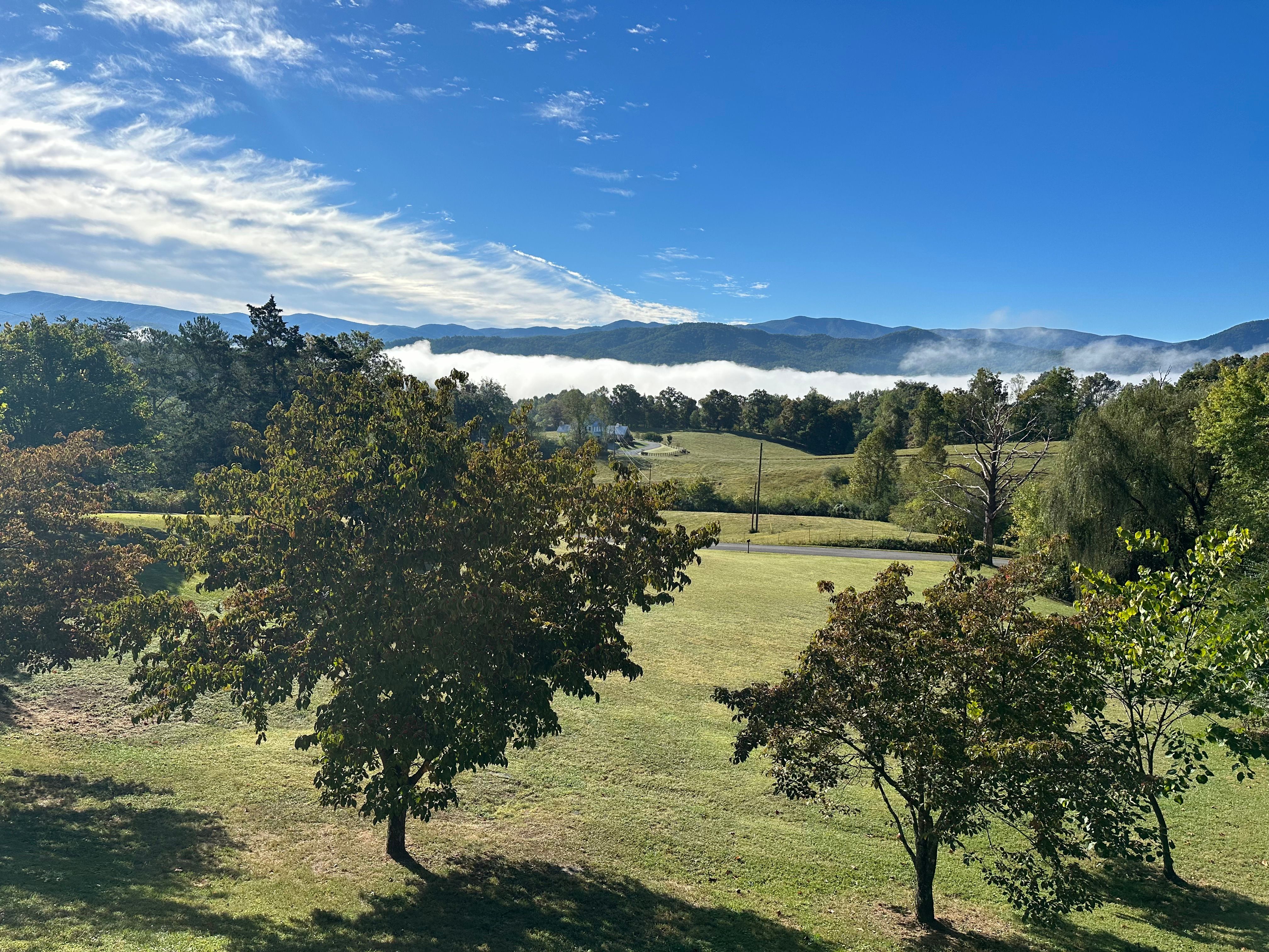 Fog lying in the valley below Cedar Creek Manor’s porch at dawn, with the layered blue ridgelines of the Great Smoky Mountains beyond