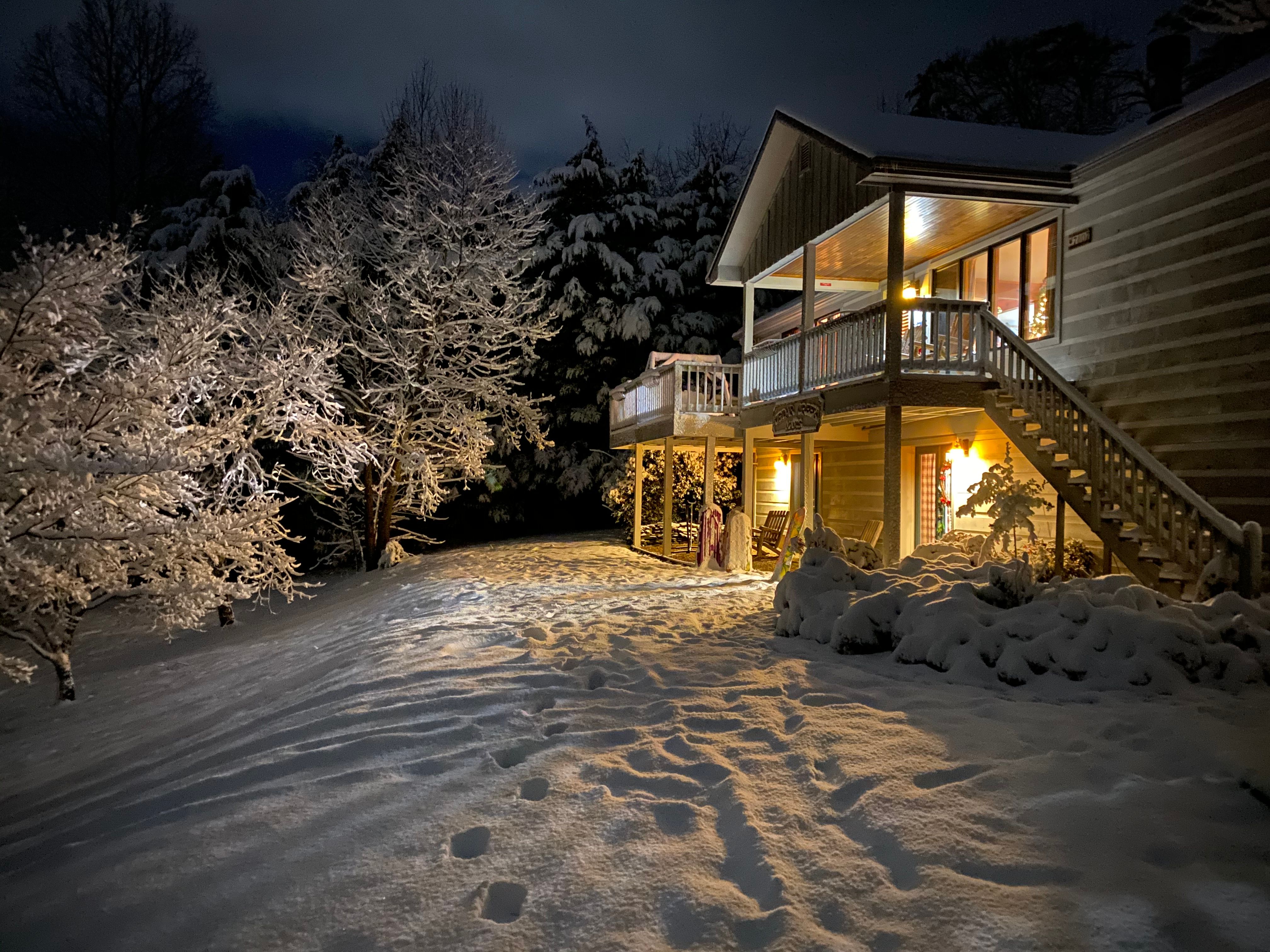 The cabin at night in the snow, windows glowing warm